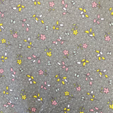 A grey cotton with a small floral print in pink and yellow all over the fabric with a speckled white spot. Kayes Textiles Fabrics.