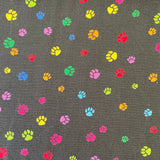 A black cotton fabric with small paw prints all over in different rainbow colours. Kayes Texiles Fabrics.