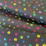A black cotton fabric with small paw prints all over in different rainbow colours. Kayes Texiles Fabrics.