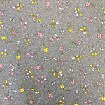 A grey cotton with a small floral print in pink and yellow all over the fabric with a speckled white spot. Kayes Textiles Fabrics.