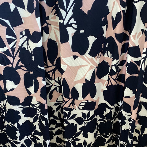 A silky polyester jersey with a dusky pink base with navy and white floral silhouette design. A white and navy floral design border at the bottom of the fabric. Kayes Textiles fabric