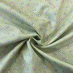 A light sage cotton with a small floral print in pink, blue and yellow all over the fabric with a speckled white spot. Kayes Textiles Fabrics.