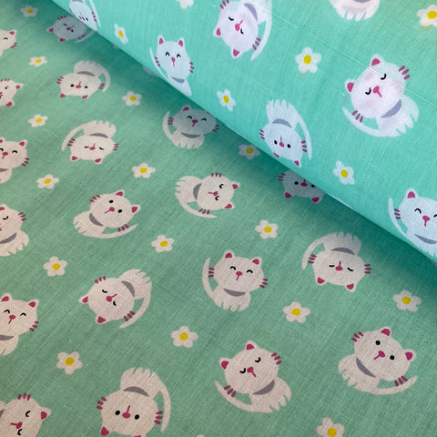 A mint coloured fabric with small white cartoon cats all  over. Kayes Textiles Fabrics