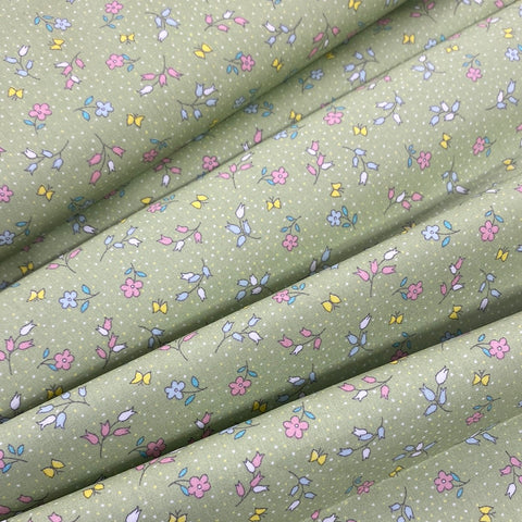 A light sage cotton with a small floral print in pink, blue and yellow all over the fabric with a speckled white spot. Kayes Textiles Fabrics. 