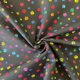 A black cotton fabric with small paw prints all over in different rainbow colours. Kayes Texiles Fabrics.