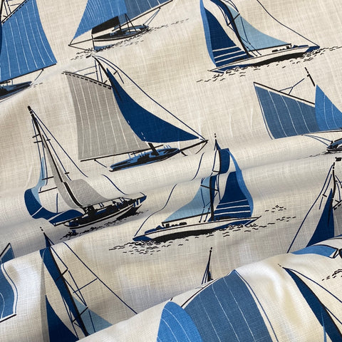 A white cotton fabric with sailing boats all over in shades of blue and grey. Kayes Textiles Fabrics.